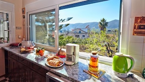 Eine Küche mit einem großen Fenster, einer Kaffeemaschine, einem grünen Wasserkocher und einem Teller mit Essen.