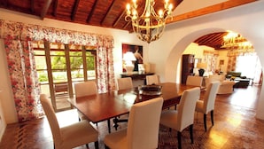 Un comedor con mesa y sillas de madera, una araña y cortinas con motivos florales.