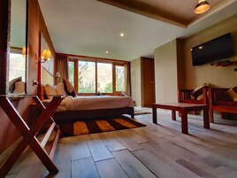 Un dormitorio con cama, escritorio, silla, televisor y ventanas amplias.
