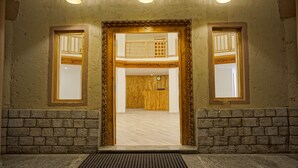 Entrada de hotel com porta de madeira, duas janelas laterais e parede de pedra.