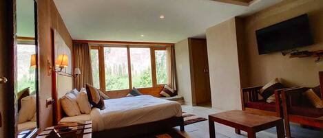 A bedroom with a bed, a wooden bench, a TV mounted on the wall, and large windows.