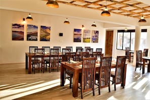 Un espace repas avec des tables et des chaises en bois, des œuvres d’art accrochées aux murs et des luminaires suspendus.