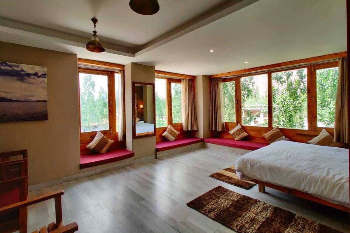 A spacious bedroom with large windows, a bed, a bench, and a wooden floor.