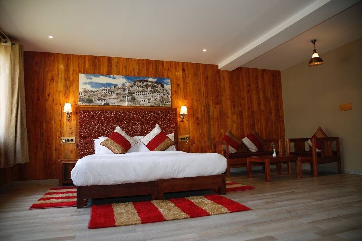 A bedroom with a wooden headboard, a large bed with white bedding, two bedside lamps, and a red and beige striped rug.
