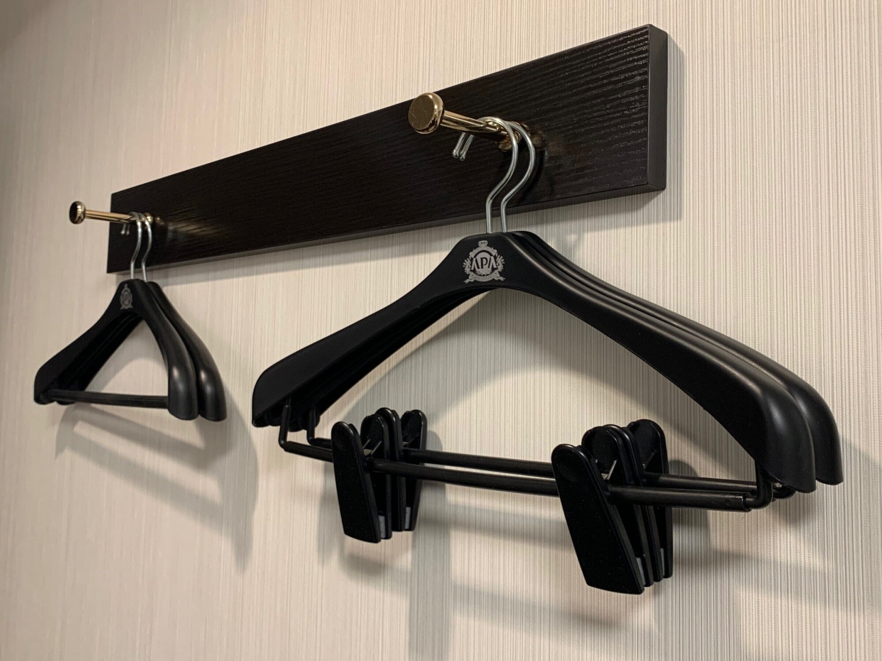A wall-mounted coat rack with two black hangers and a black shelf.