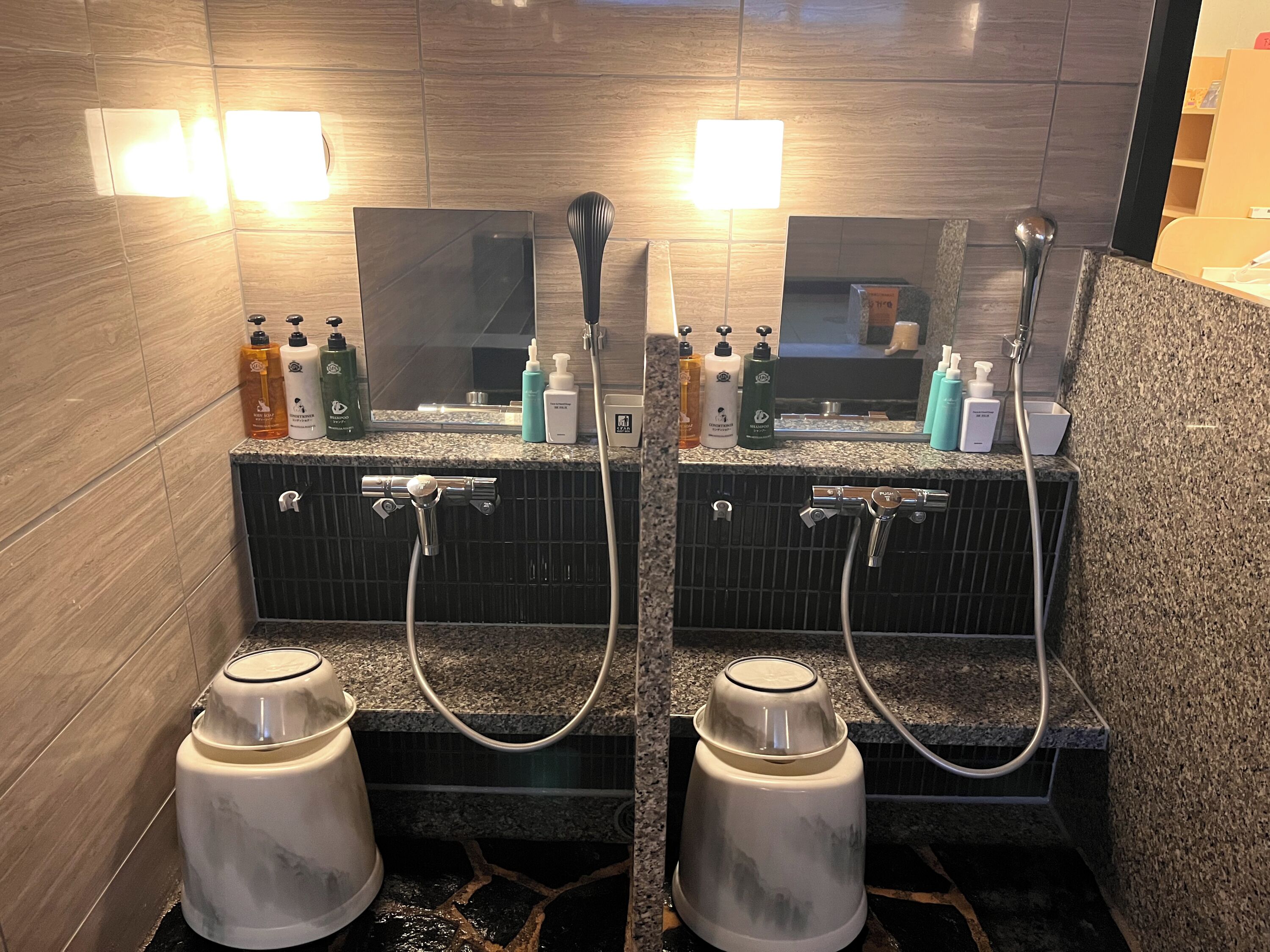 A bathroom with two sinks, each with a mirror, towel dispenser, and hand soap. There are two showerheads and a white pedestal sink.