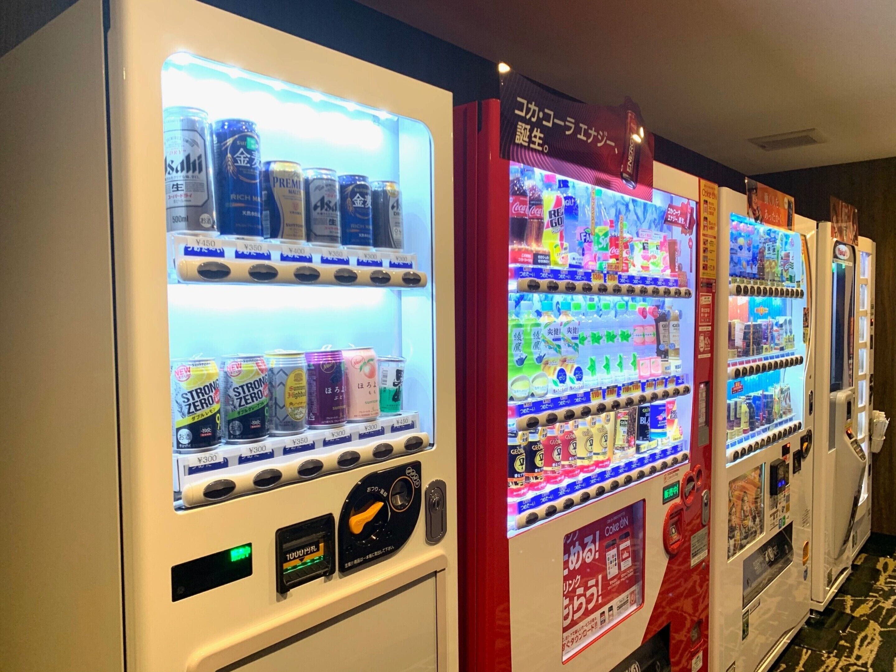 Automat mit verschiedenen Getränken und Snacks, darunter Dosen und Flaschen, in einer gewerblichen Umgebung.
