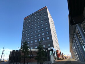 En hög byggnad med skylten ”APA HOTEL” på toppen och en skylt med japanska tecken längst ner.