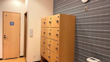 Habitación de hotel con una puerta de madera que indica "Toilet", varios taquillones de madera, un reloj en la pared y un enchufe.