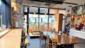 A restaurant with a large wooden table, several chairs, and a bench. There is a counter with a coffee machine and various decorations. - APA Hotel Joetsu Myoko Ekimae (Joetsu)