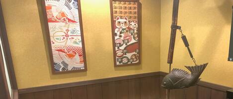 A restaurant interior with wooden paneling, a fish-shaped hanging light, and two decorative panels with Asian motifs.