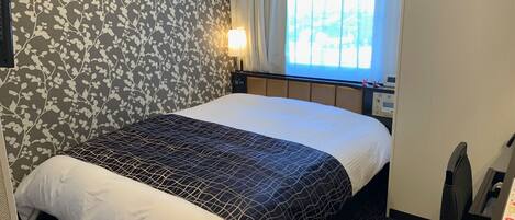 A hotel room with a bed, a nightstand, a lamp, and a window with curtains.