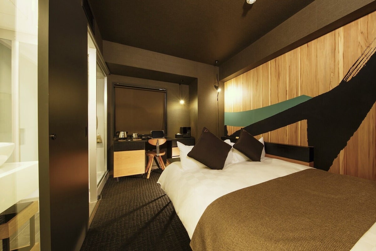 A hotel room with a bed, desk, and a view of the outside.
