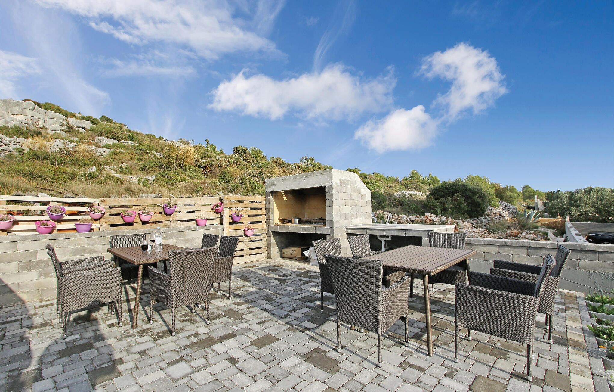 An outdoor patio with wicker furniture, a stone barbecue, and potted plants.