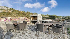 Une terrasse extérieure avec des meubles en osier, un barbecue en pierre et des plantes en pot.