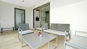 Un espace d’attente moderne avec deux fauteuils gris rembourrés, une petite table sur laquelle se trouve un récipient rouge, et une cloison en verre.