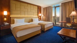 A hotel room with two beds, a desk, and a view of the city. - New Tiflis Hotel (Tbilisi)