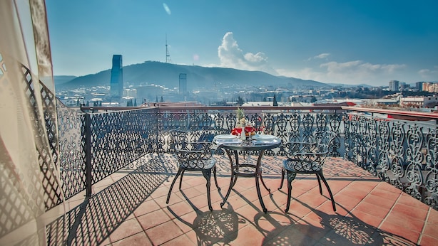 A terrace with a table and chairs, overlooking a cityscape with mountains and a tall building. - New Tiflis Hotel (Tbilisi)