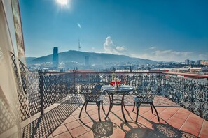 A terrace with a table and chairs, overlooking a cityscape with mountains and a tall building. - New Tiflis Hotel (Tbilisi)