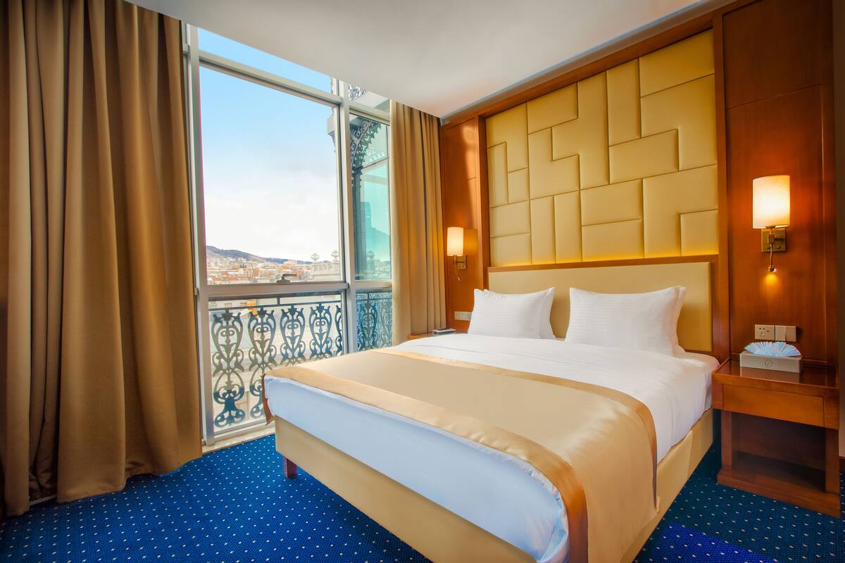 A hotel room with a large bed, a view of the city, and a balcony with curtains.