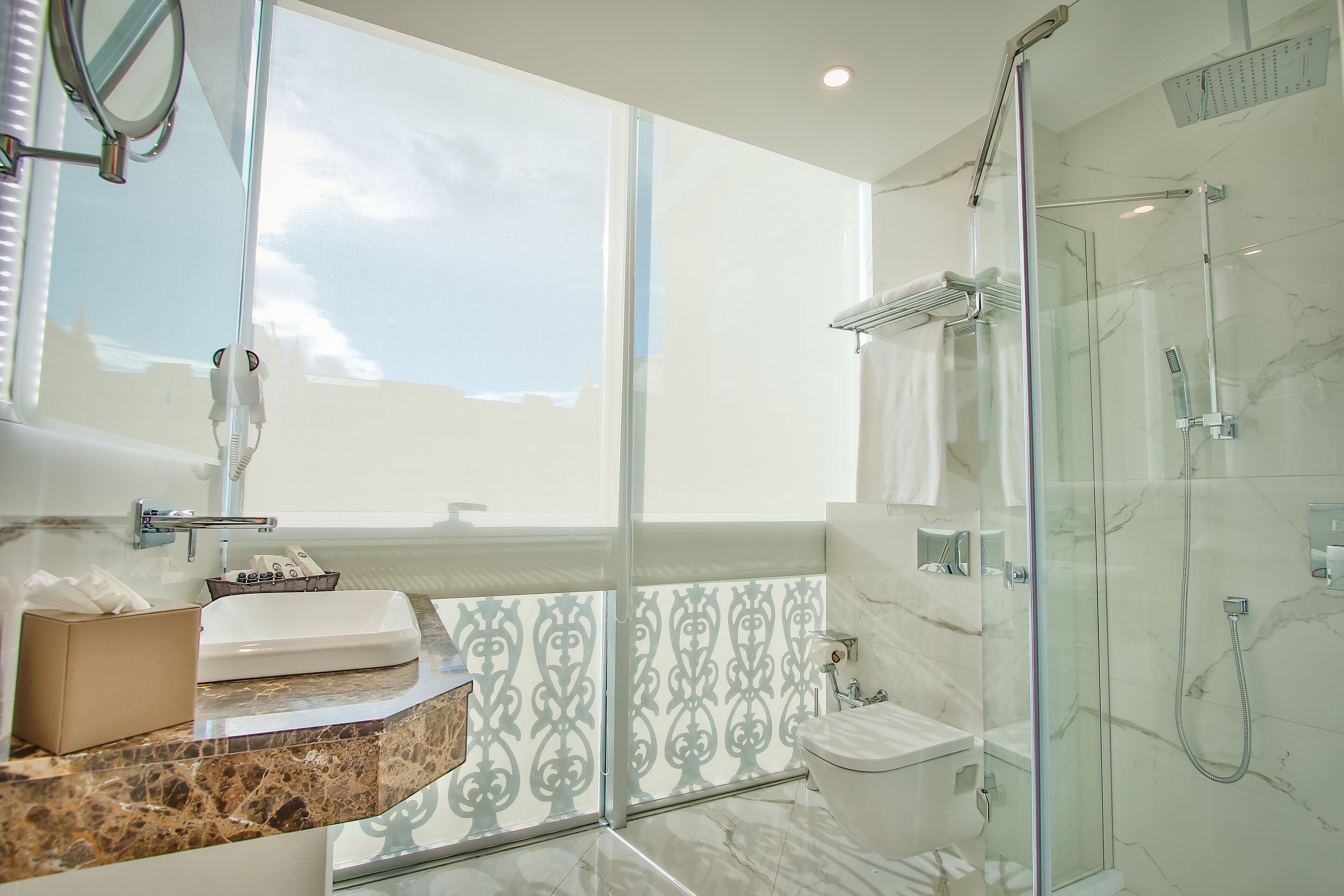 A modern bathroom with a glass shower enclosure, a large window, and a marble countertop.