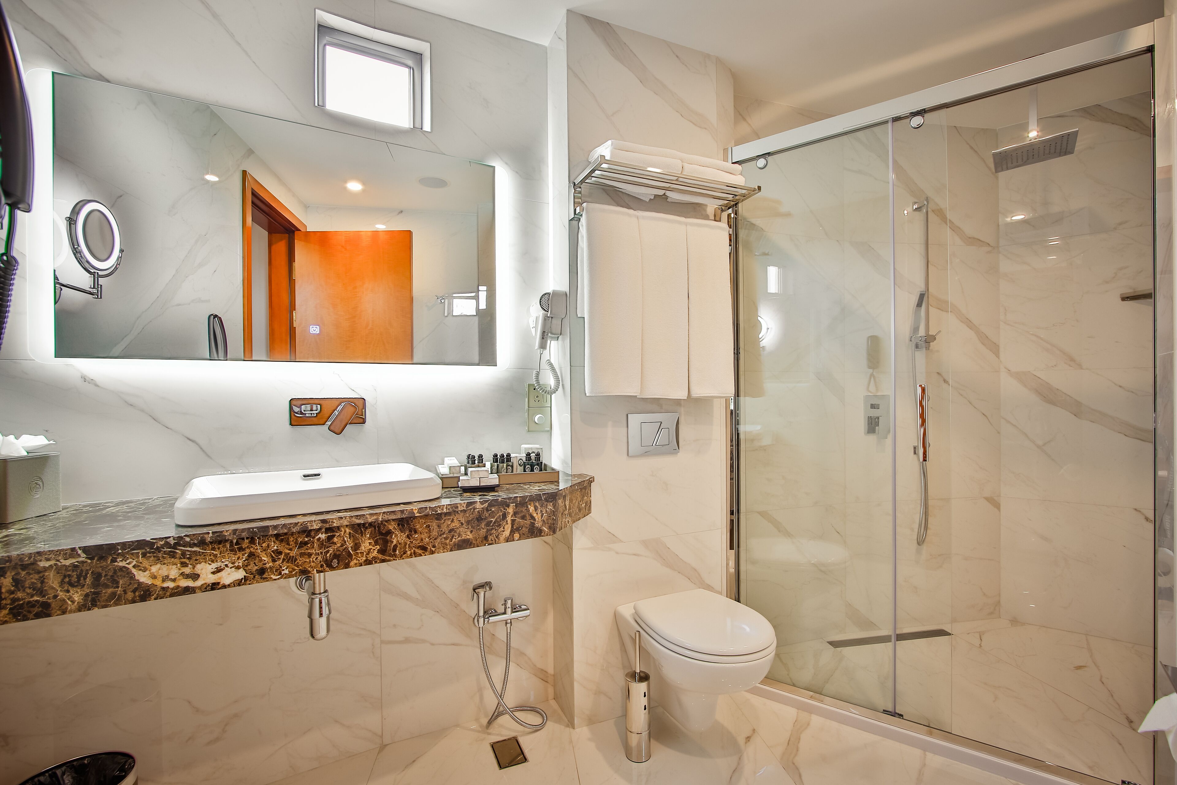 Een moderne badkamer met een marmeren wastafel, een douche met glazen wanden en een toilet.