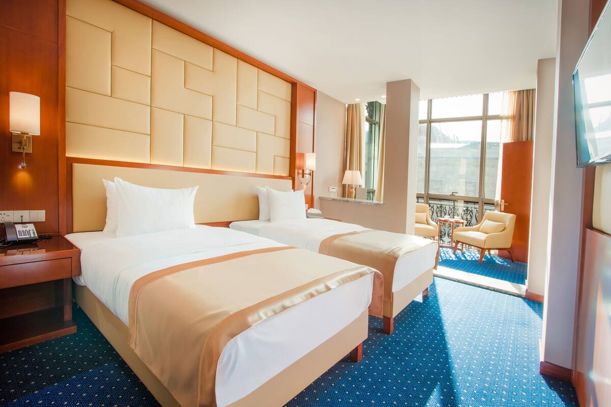 A hotel room with two beds, a desk, a chair, and a large window.