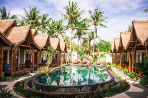 Un complexe hôtelier doté de bungalows aux toits de chaume, d’une piscine centrale et de palmiers.