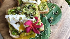 A wooden board with toast topped with avocado, seeds, and a flower. - Gili One Hotel & Resort (Gili Trawangan)