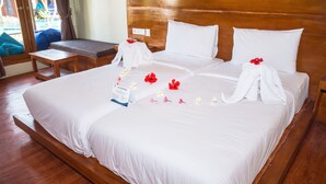 A neatly made bed with white linens, a wooden headboard, and a small bedside table with a book and a towel. - Gili One Hotel & Resort (Gili Trawangan)