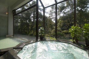 A hot tub with a view of a forest through large windows. - Akiu Resort Hotel Crescent (Sendai)