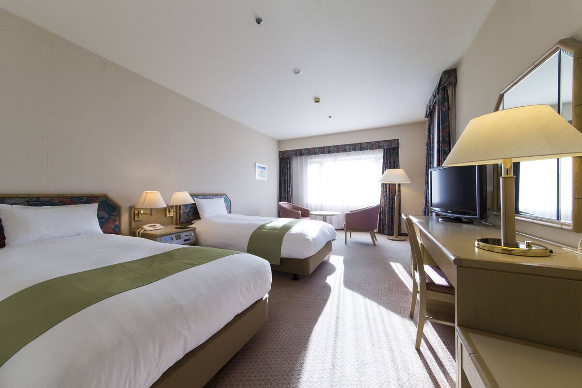 A hotel room with two beds, a desk, a chair, a television, and a large mirror.