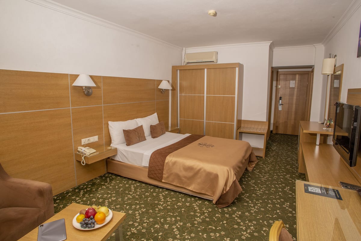 A hotel room with a bed, bedside table, lamp, wardrobe, TV, and a small desk with a chair.