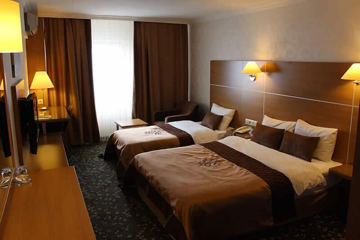 A hotel room with two beds, a desk, a chair, and a television.