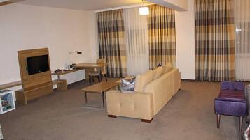 Een woonkamer met een bank, een salontafel, een televisie en gordijnen.