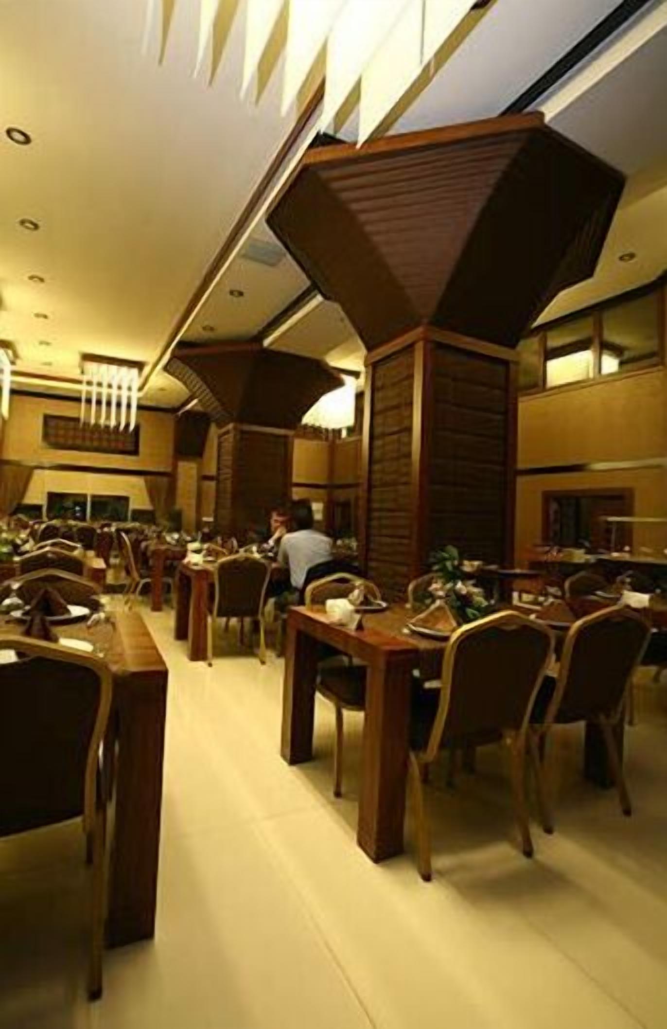 A spacious dining area with multiple tables and chairs, wooden paneling on the walls, and a warm ambient lighting.