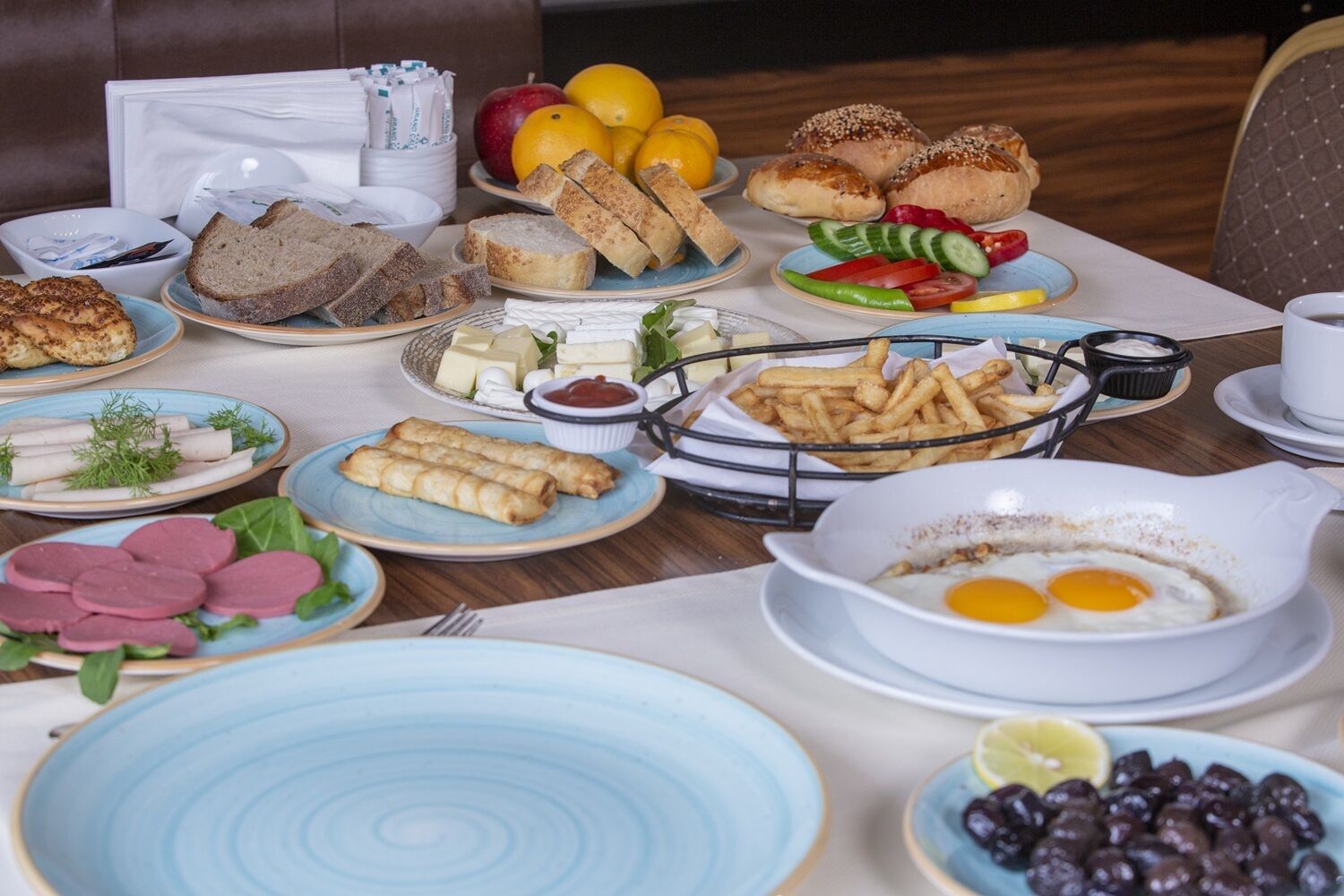 A breakfast buffet with various dishes including bread, eggs, sausages, and fruits.