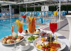 A poolside dining area with tables set for guests, a pool in the background, and various food and drink options. - Grand Cali Hotel (Bozuyuk)