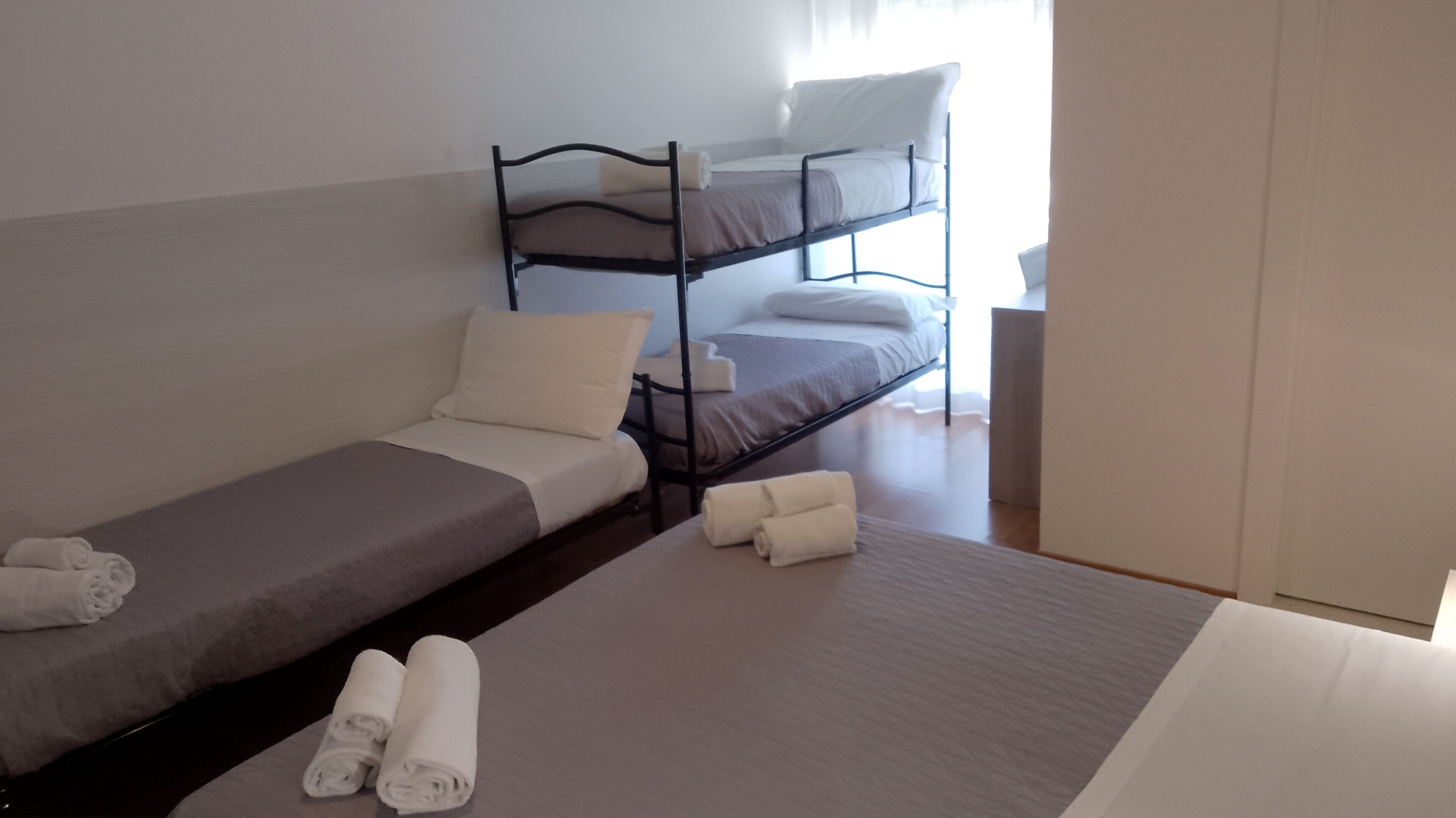 Ein Zimmer mit einem Einzelbett, einem Schlafsofa und einem Etagenbett. Auf dem Boden liegen zusammengerollte Handtücher.