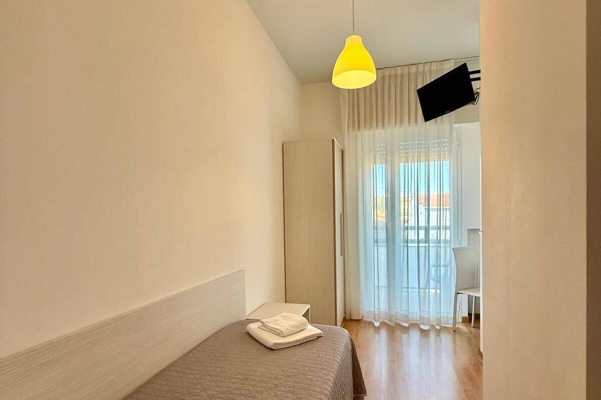 A hotel room with a bed, a desk, and a chair. There is a window with curtains and a view of the outside.