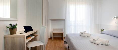 Ein modernes Hotelzimmer mit einem Holztisch, einem Stuhl, einem Bett mit ordentlich gefalteten Handtüchern und einem kleinen Nachttisch.