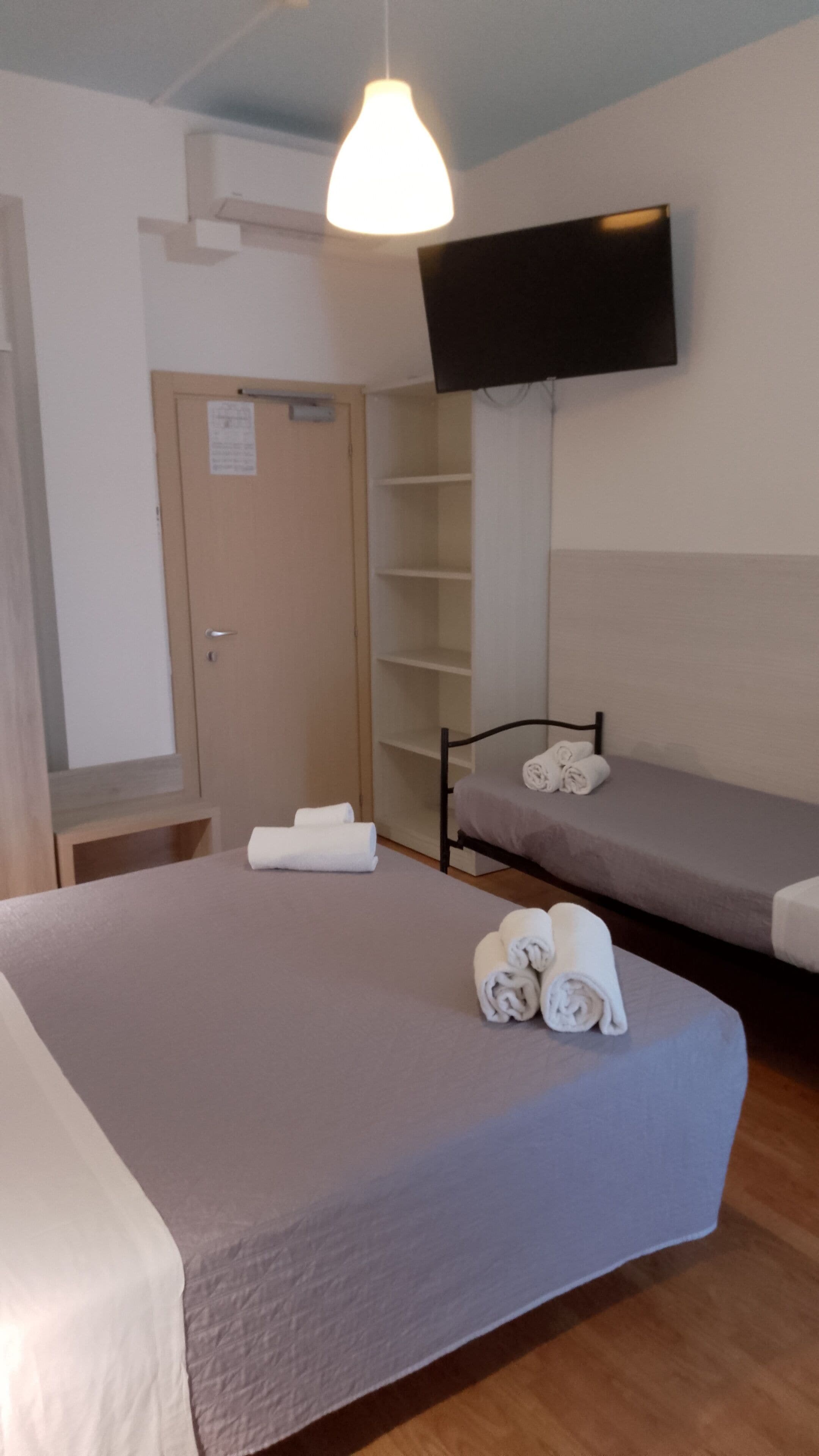 A bedroom with a bed, a bedside table, a TV, a wardrobe, and a shelf.