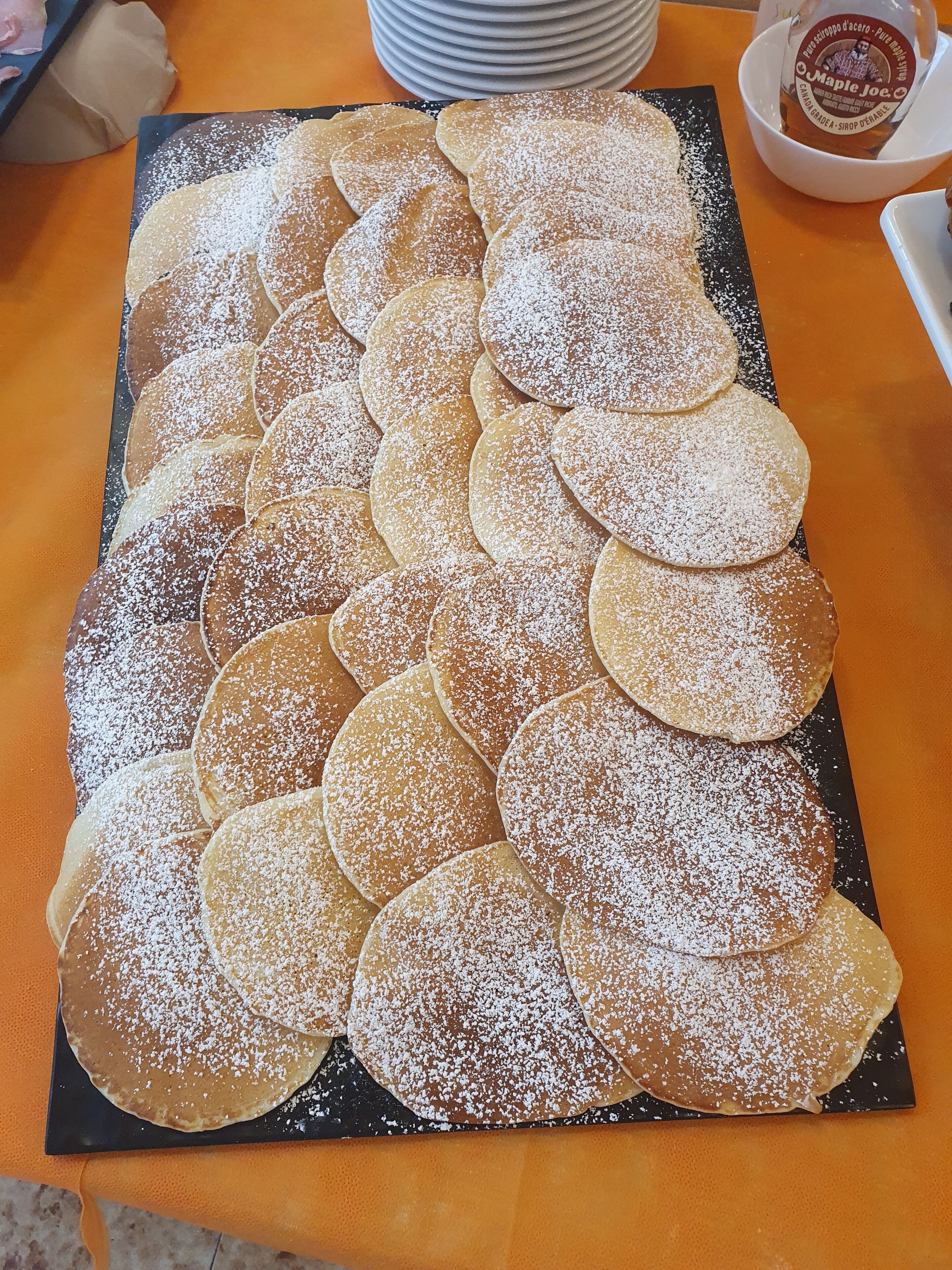 A tray of crepes dusted with powdered sugar, arranged on a black plate.