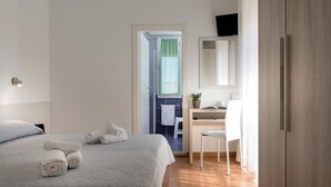 A hotel room with a bed, a desk with a chair, a television, and a bathroom visible through an open door.