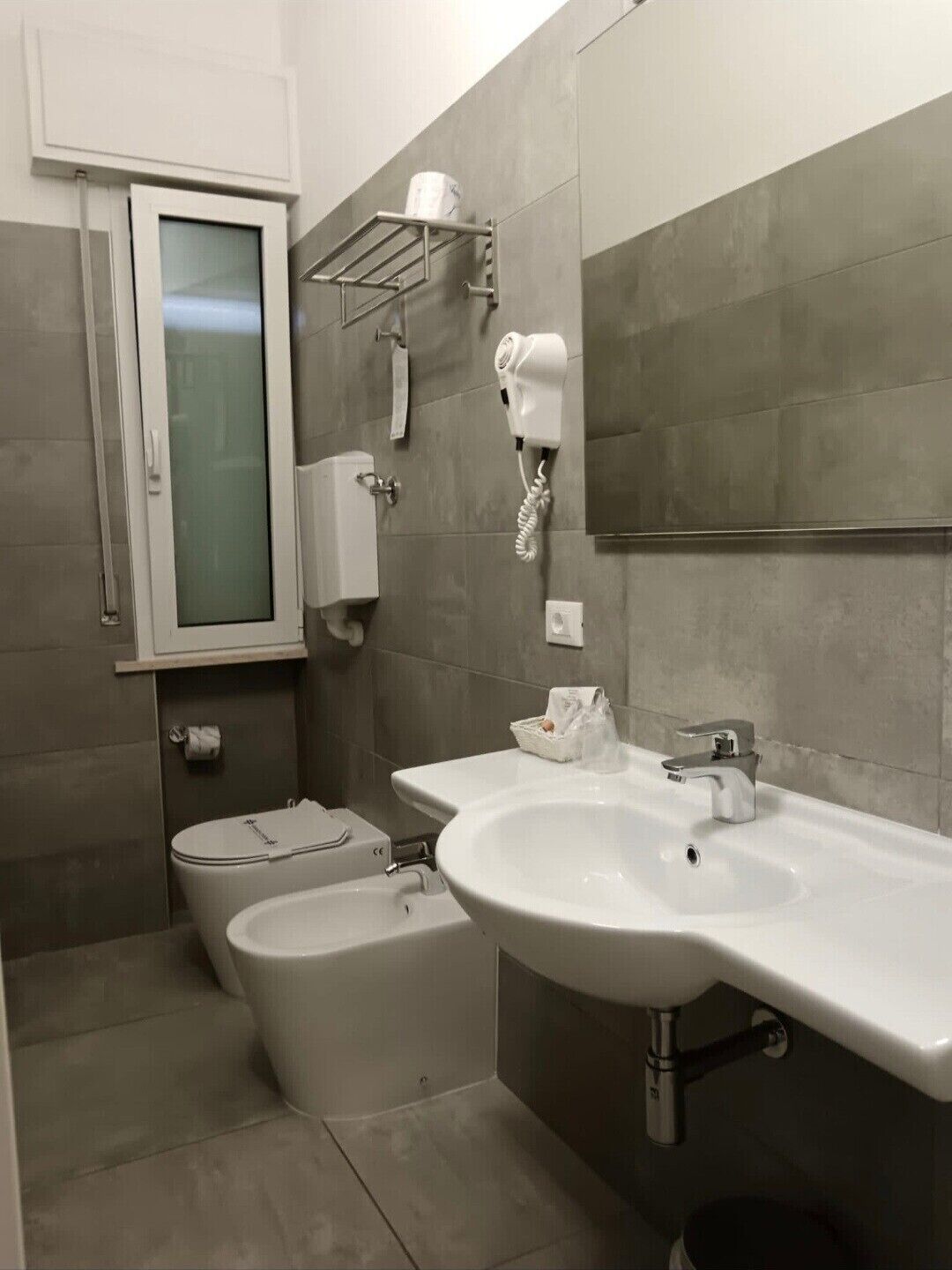 Une salle de bain moderne équipée de toilettes, d’un bidet, d’un lavabo et d’un sèche-cheveux fixé au mur.