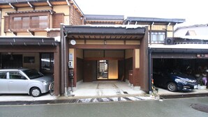 A traditional Japanese building with a covered entrance, a car parked inside, and another car parked outside.