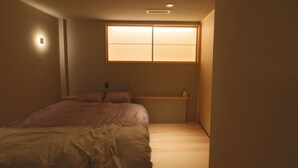 A bedroom with a bed, a nightstand, a shelf, and a window with a light.