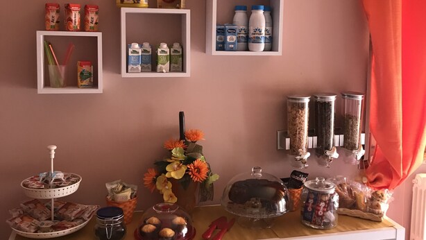 Une petite cuisine équipée de divers produits alimentaires, d’une machine à café et d’étagères de rangement.