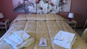 Un lit bien fait, recouvert d’une couverture dorée, avec deux serviettes pliées et un livre intitulé « Il Piccolo Principe » posé sur le lit.