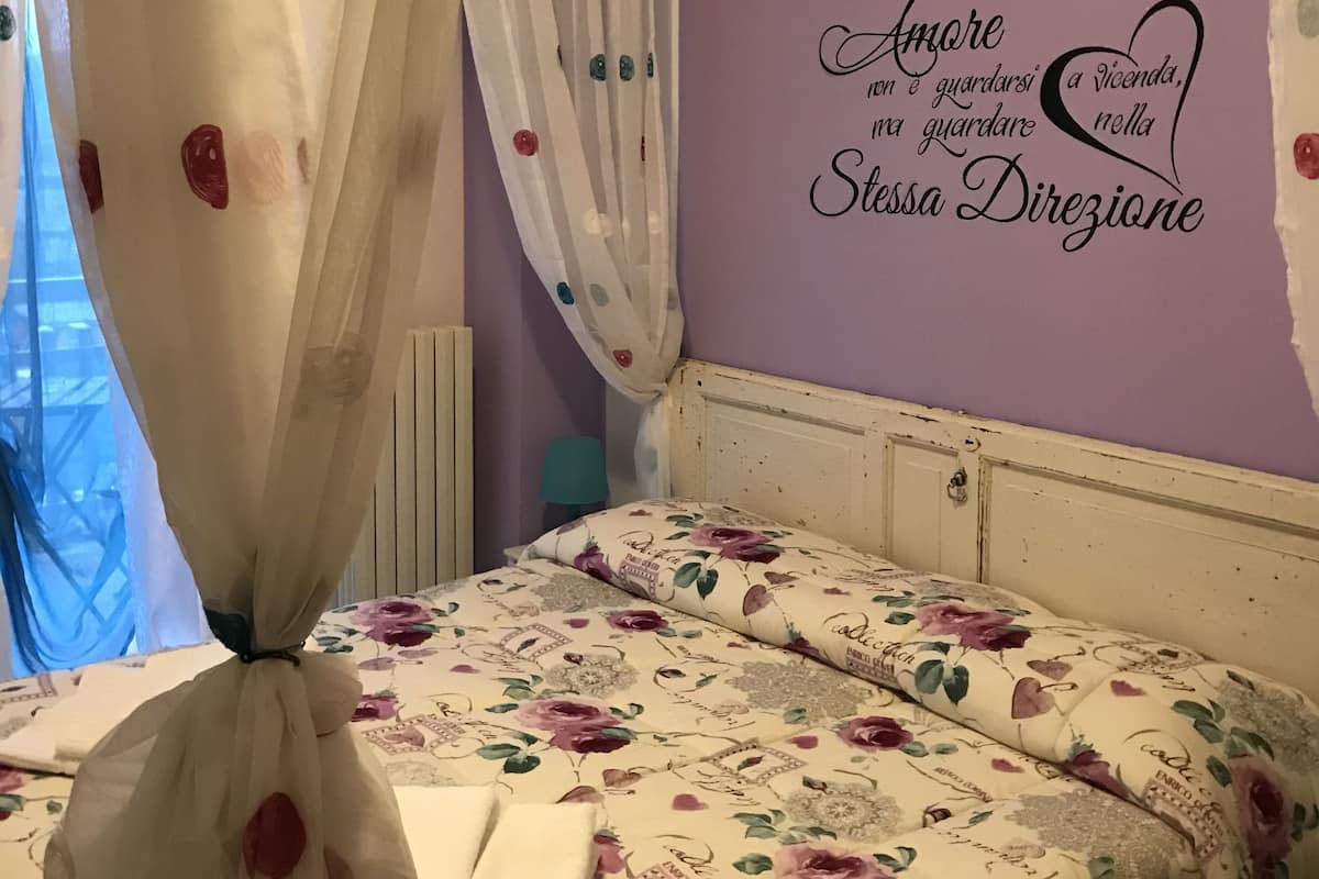 A bedroom with a bed, a purple wall with a decorative phrase, and a window with a curtain.